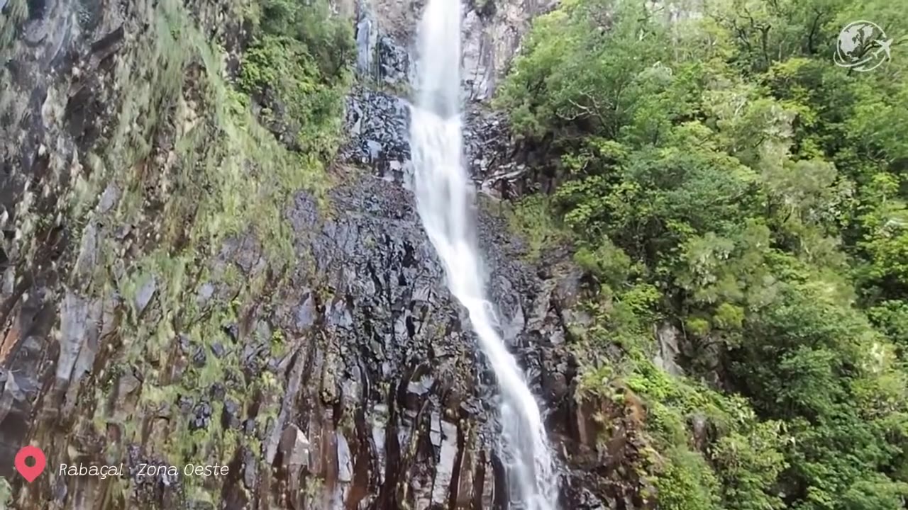 Caminhantes a percorrer o estreito trilho da Levada das 25 Fontes, ladeado por pedras, através da floresta de loureiros da Madeira