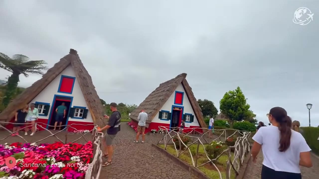 Fileira de casas de Santana com telhados triangulares de palha, pintadas de branco e vermelho, ao lado dos jardins da prefeitura, na Madeira